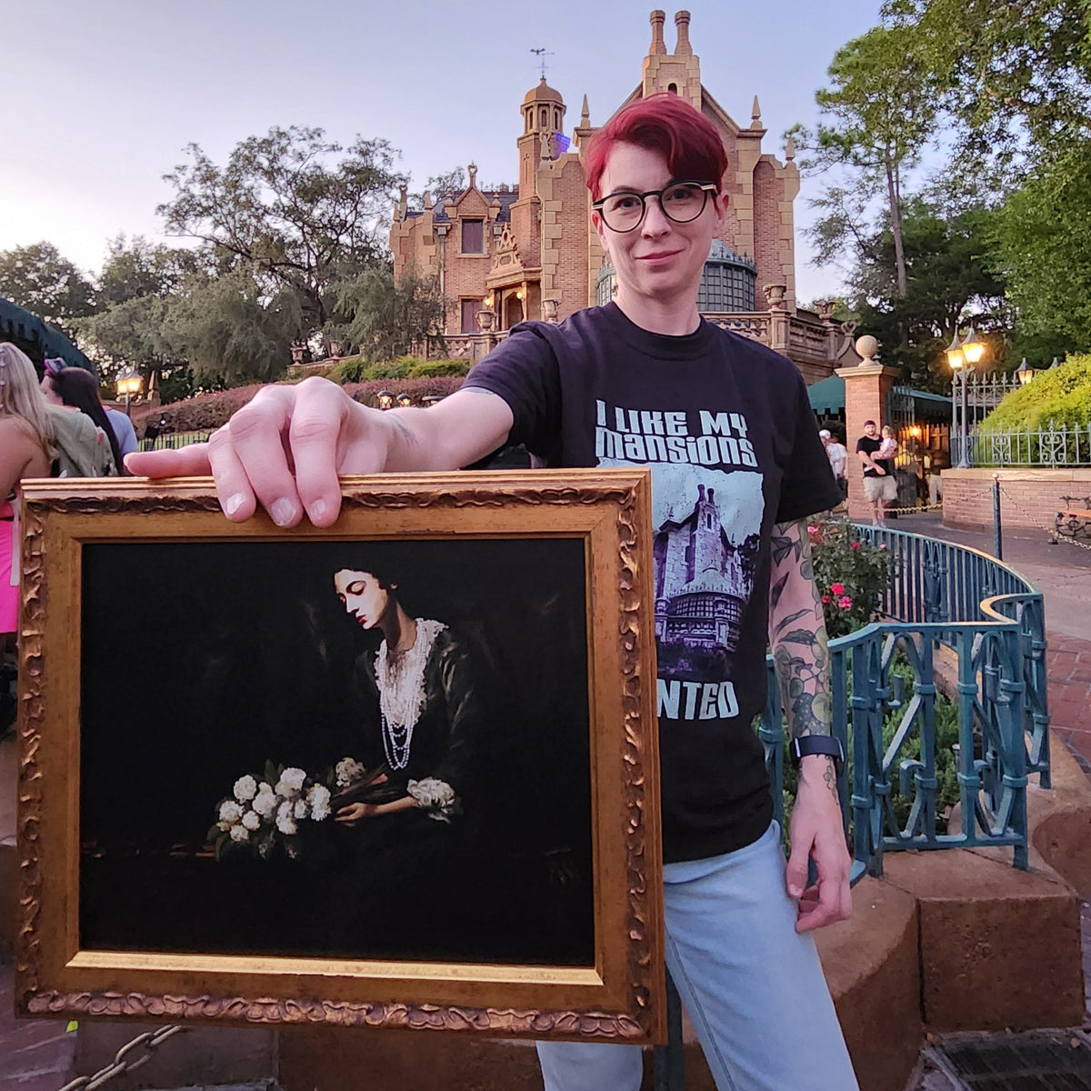 Kylie holding the framed Constance Hatchaway Fine Art Print outside the Haunted Mansion at dusk