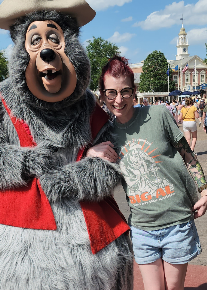 Kylie in the Big Al On The Frontier Tee in Blue Spruce posing with Big Al in Magic Kingdom