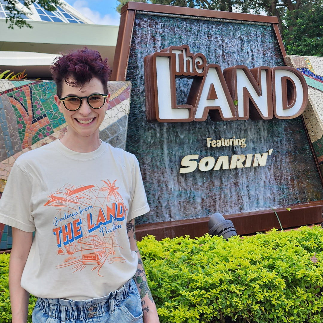 Kylie wearing the Land Pavilion Tee in Ivory in front of The Land sign featuring Soarin&