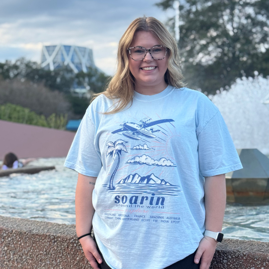 Soarin' Around the World Tee in Chambray worn by a smiling woman in front of a fountain at EPCOT
