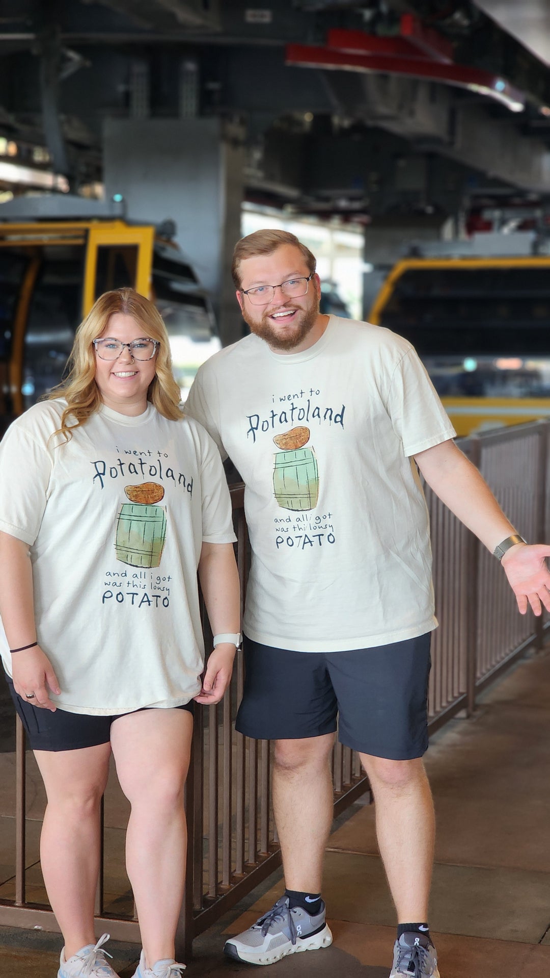 Couple wearing matching Potatoland Tees in Ivory, standing together inside a Hollywood Studios queue area