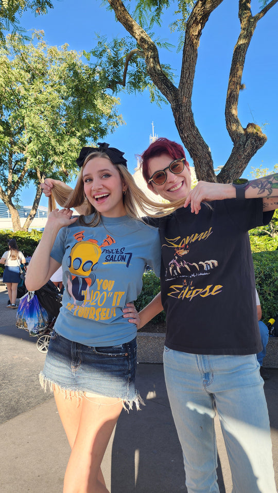 Sonny Eclipse Tee worn by a woman with short red hair posing with a friend under a tree in the park