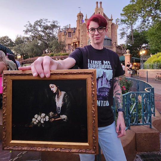 Kylie holding the framed Constance Hatchaway Fine Art Print outside the Haunted Mansion at dusk