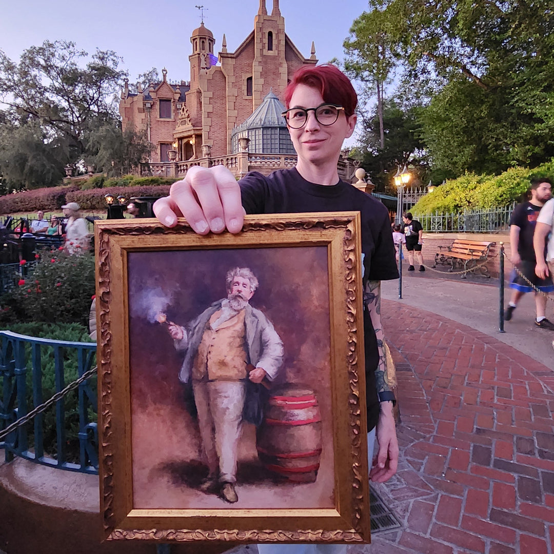 Artist Kylie Bodiya holding a framed picture with Dynamo from the Haunted Mansion Stretching room with the haunted mansion in the background