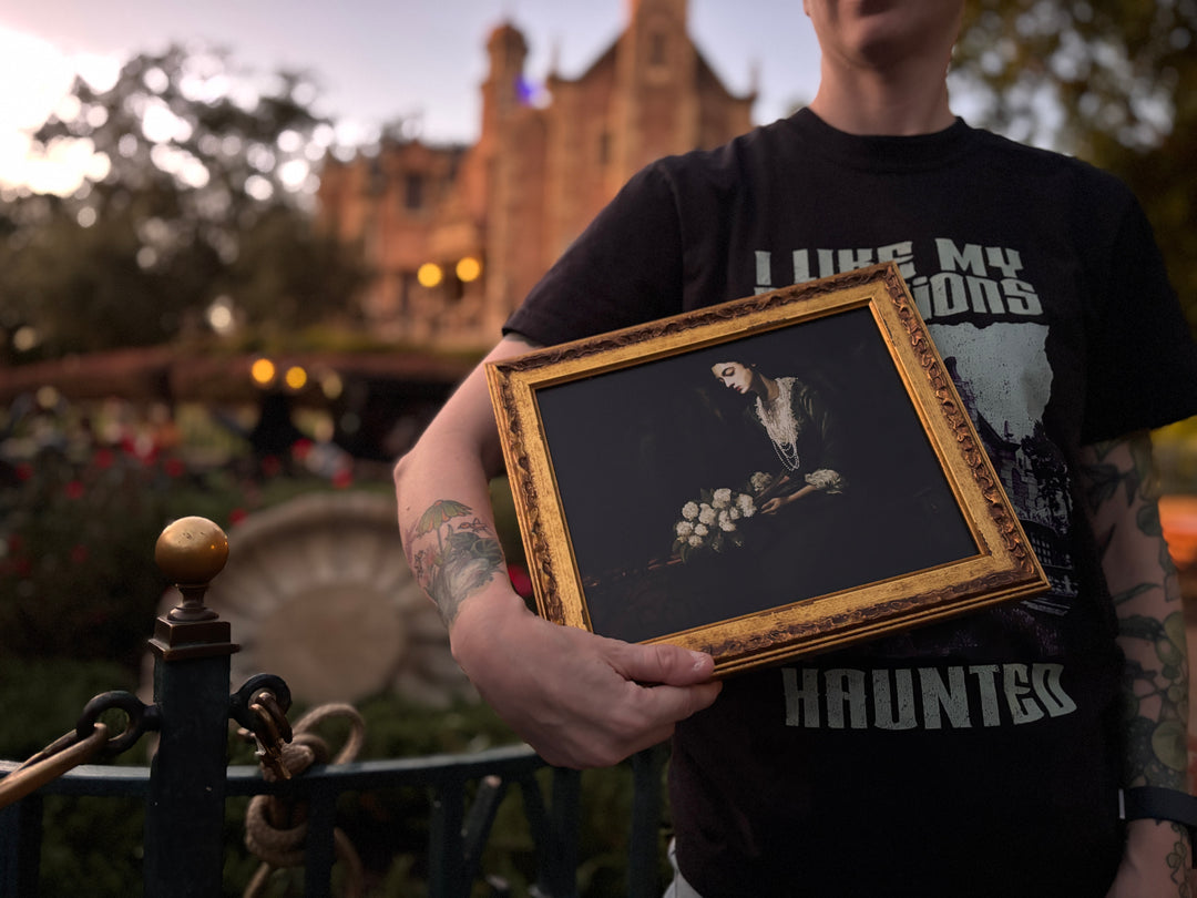 Constance Hatchaway Fine Art Print in a small gold frame held in front of the Haunted Mansion, close-up