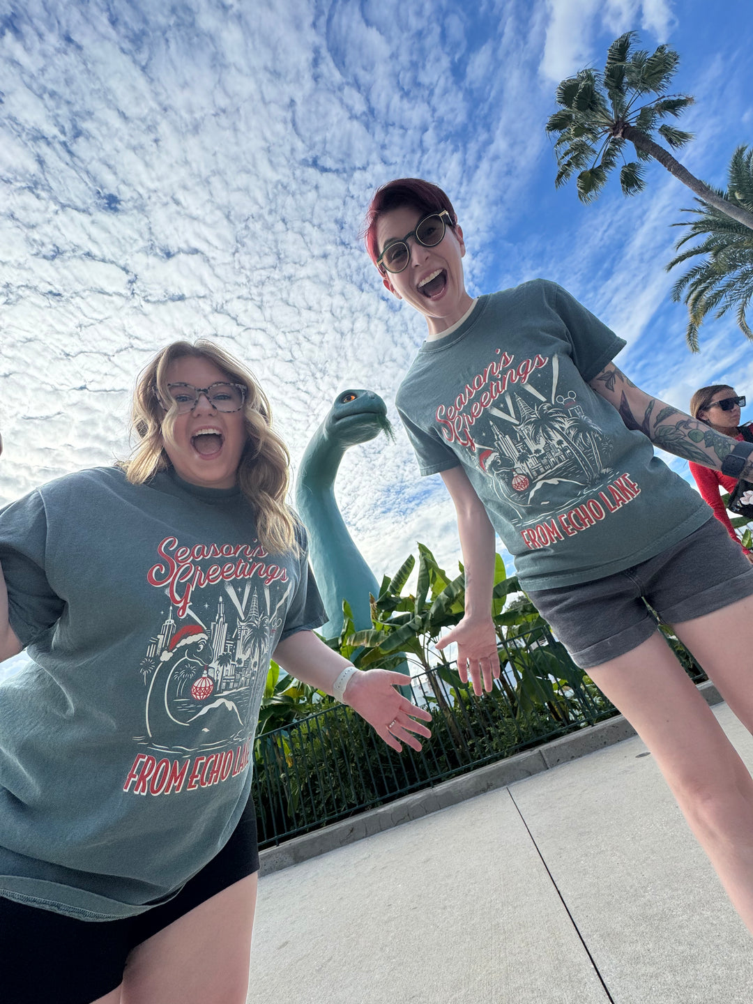 Two women in matching Echo Lake Christmas Shirts posing with Gertie the dinosaur at Hollywood Studios