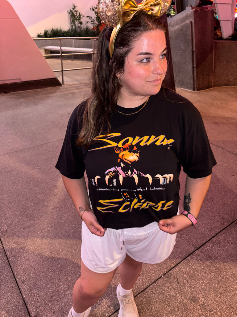 Sonny Eclipse Tee worn by a smiling woman in Minnie ears and white shorts, looking aside at dusk in Tomorrowland