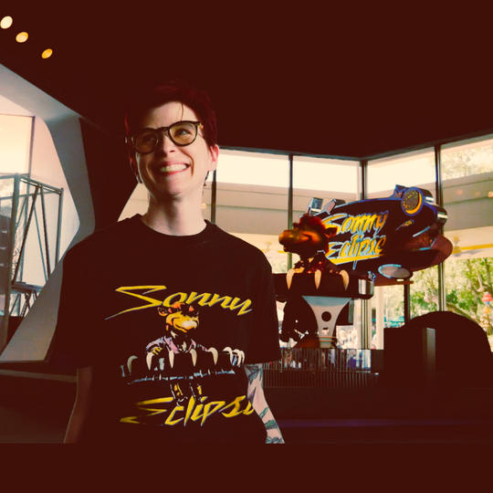 Kylie in the Sonny Eclipse Tee standing in front of the Sonny Eclipse animatronic at Cosmic Ray's