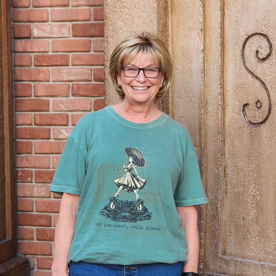 Sally Slater Haunted Mansion Shirt worn by a smiling woman in glasses against a brick and stone wall