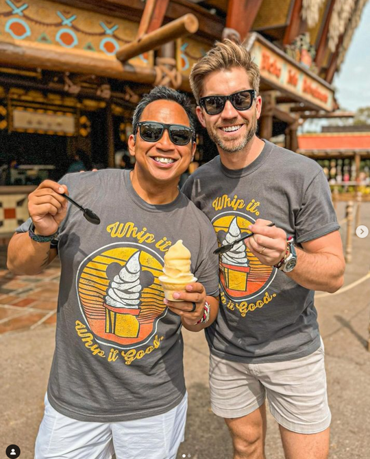 Dole Whip Tee in Graphite worn by two men in sunglasses holding Dole Whips in Adventureland