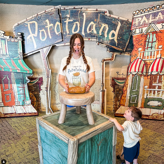 Potatoland Tee in Ivory worn by a woman lifting a potato at the Potatoland photo spot while a toddler looks on
